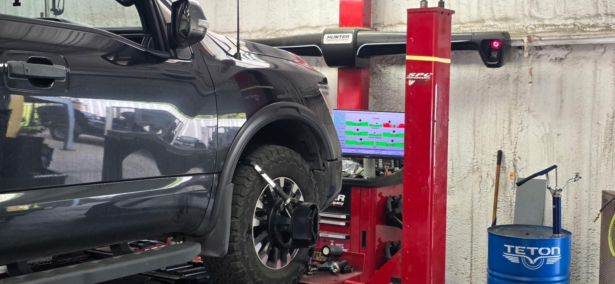 A truck on the alignment rack at Complete Automotive Repair, with a sensor head clamped to the front wheel and the alignment readout on screen behind it